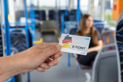 Hand h&auml;lt ein D-Ticket im Bus, Fahrgast im Hintergrund.